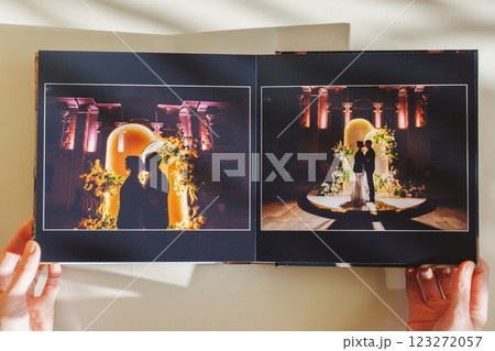 Female hands flipping through a photo book with wedding photos on a white table 123272057