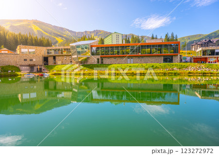 At Jasna Ski Resort in the Low Tatras, the summer landscape features vibrant greenery and serene water, reflecting the modern architecture of the resort against a stunning mountainous backdrop. 123272972