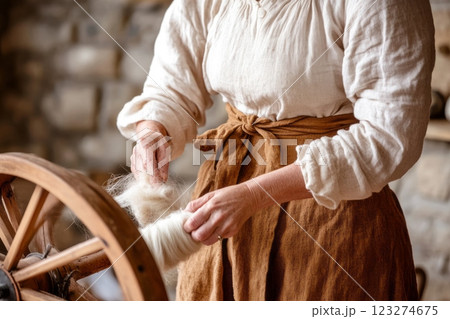 A woman working with a spinning wheel, creating yarn from raw wool in a rustic, historical setting. 123274675