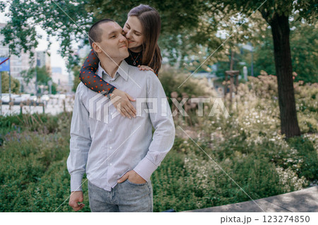 Happy couple in love enjoying a playful moment in the city park. A young man sitting on a bench holding his girlfriend in his arms as they smile at each other. Urban nature, romance, and joy. 123274850