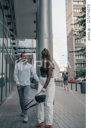 Romantic couple embracing and sharing a kiss in an urban setting. Young stylish man and woman in trendy outfits enjoying a moment of love on a city sidewalk. Modern architecture in the background. 123274878