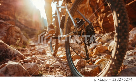 Close-up of mountain bike wheel and gears on rocky terrain at golden hour. Detailed view of bicycle mechanism with dramatic sunlight creating warm atmosphere on mountain trail Close-up of mountain bike wheel and gears on rocky terrain at golden hour. Detailed view of bicycle mechanism with dramatic sunlight creating warm atmosphere on mountain trail 123276274
