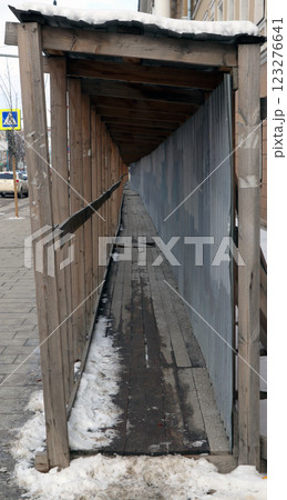 Long pedestrian passageway with wooden boards during building restoration in winter 123276641