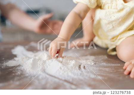 Close-up cropped shot of unrecognizable curious toddler girl playfully scattering flour, capturing joyful moments of childhood exploration sitting on table, learning through play, sensory exploration. Close-up cropped shot of unrecognizable curious toddler girl playfully scattering flour, capturing joyful moments of childhood exploration sitting on table, learning through play, sensory exploration. 123276738