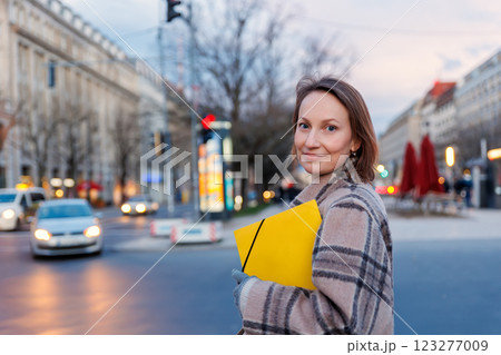Happy woman portrait holding yellow folder papers document letter on european busy Berlin Mitte city street twilight evening night. Female student business  person journey visiting Germany capital 123277009