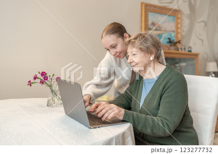 Young woman helping a senior woman with using laptop at home. Concept of technology, education, and senior digital adaptation. Granddaughter teaches grandmother how to use digital device. Young woman helping a senior woman with using laptop at home. Concept of technology, education, and senior digital adaptation. Granddaughter teaches grandmother how to use digital device. 123277732