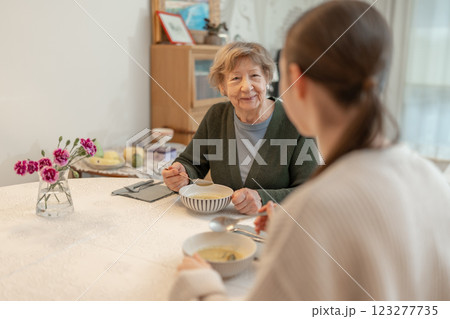 Elderly woman enjoying meal with younger female family member at home. Concept of family bonding, aging, and healthy eating. Grandmother spending quality time with granddaugther at home.  123277735