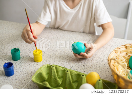 The hands of a child coloring eggs with a brush. Nearby are paints and a wicker basket. Easter 123278237