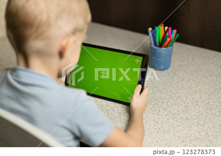The child is sitting at the table, playing and looking at the tablet on the green screen. Chromakey The child is sitting at the table, playing and looking at the tablet on the green screen. Chromakey 123278373