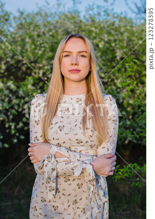 Blonde girl with her arms crossed looks directly into the camera against the background of a blooming green garden. Cover photo Blonde girl with her arms crossed looks directly into the camera against the background of a blooming green garden. Cover photo 123278395