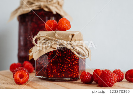 Delicious homemade raspberry jam presented in charming jar on a rustic wooden board, adorned with paper and twine. Fresh raspberries add a pop of color. Delicious homemade raspberry jam presented in charming jar on a rustic wooden board, adorned with paper and twine. Fresh raspberries add a pop of color. 123278399