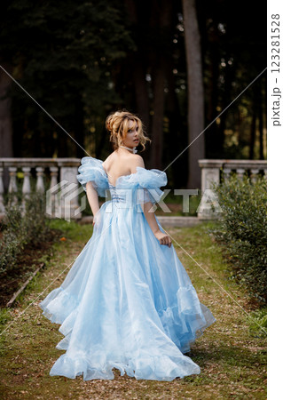 Romantic Woman in a Light Blue Gown Posing on a stone balustrade in a picturesque garden. 123281528