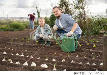 Young man with boy planting seeds in field 123282175