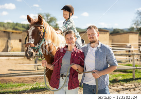 Father, mother and son riding horse together at small horse farm Father, mother and son riding horse together at small horse farm 123282324