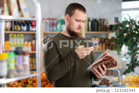 Male shopper scanning QR code on ham label in grocery department of supermarket Male shopper scanning QR code on ham label in grocery department of supermarket 123282343