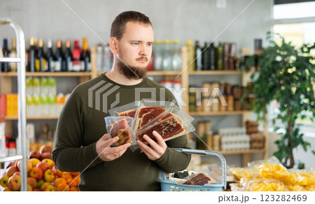 Shopping in supermarket - male buyer makes a choice when buying jamon Shopping in supermarket - male buyer makes a choice when buying jamon 123282469