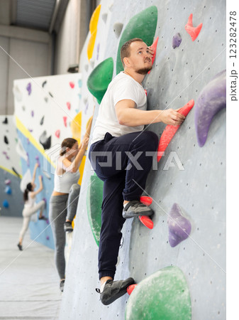 Man climbs steep artificial wall in sports complex and trains endurance and muscle strength. Active recreation in fitness center gym, types of recreation 123282478
