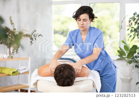 Diligent woman massage therapist massaging relaxing guy at spa complex 123282513