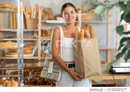 Positive young girl holding baguettes in paper bag in bakery Positive young girl holding baguettes in paper bag in bakery 123282527