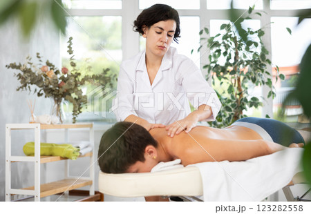 Diligent woman massage therapist massaging relaxing guy at spa complex 123282558