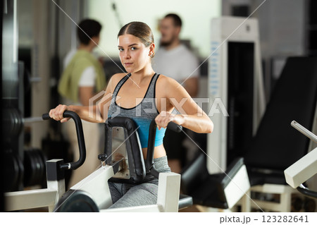 Girl in gym performs exercises for arm muscles using simulators and fitness center equipment. Girl in gym performs exercises for arm muscles using simulators and fitness center equipment. 123282641