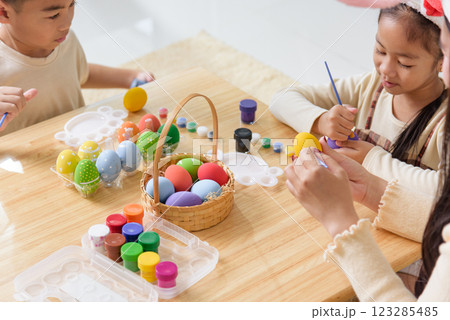 Easter fun for all. Kids with bunny ears joyfully paint Easter eggs with brushes 123285485