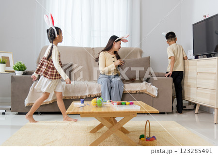 A mother and her two little children are wearing bunny ears while searching for colorful Easter eggs 123285491