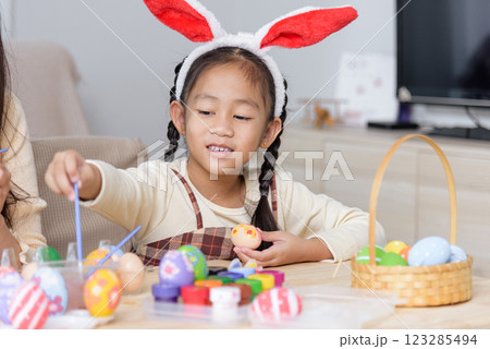 A mother and kids with bunny ears happily paint Easter eggs at a table near a festive basket 123285494
