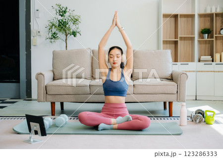 Asian Woman Doing Yoga and Watching Online Tutorials on tablet, Training 123286333