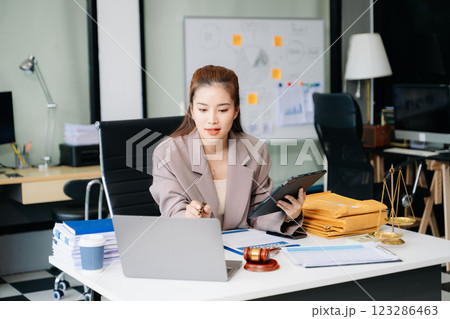 Confident lawyer working on legal analysis at a modern office desk, featuring scales of justice, a gavel Confident lawyer working on legal analysis at a modern office desk, featuring scales of justice, a gavel 123286463