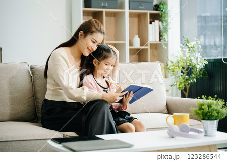 Cheerful mother and daughter sharing quality time on a couch, smiling and using a smartphone together. 123286544