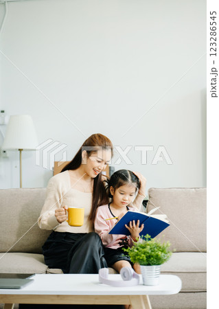 Cheerful mother and daughter sharing quality time on a couch, smiling and using a smartphone together. 123286545