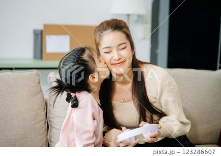 Cheerful mother and daughter sharing quality time on a couch, smiling and using a smartphone together. 123286607