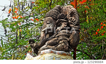An old stone statue of Ganesha covered with moss, standing on the street An old stone statue of Ganesha covered with moss, standing on the street 123290884