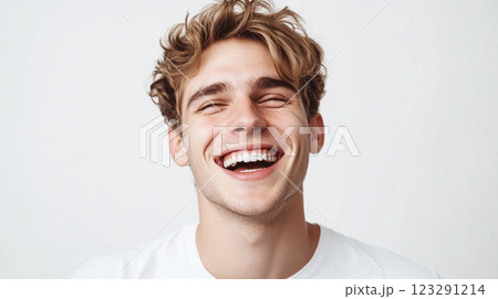 Cheerful young man with golden hair laughs wholeheartedly against a plain white backdrop, radiating joy and light. His happiness is contagious. Cheerful young man with golden hair laughs wholeheartedly against a plain white backdrop, radiating joy and light. His happiness is contagious. 123291214