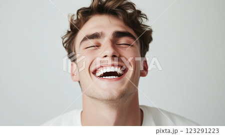 Young man expressing joy with a bright, open smile; a picture of pure happiness and carefree emotion against a simple background. 123291223