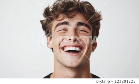 Close-up portrait of a smiling young man with curly brown hair against a clean white background, conveying joy and positive emotions. 123291225
