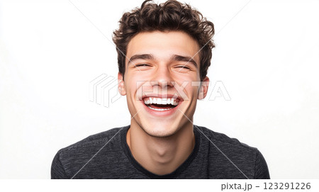 A young man with curly hair is laughing, showing his white teeth, his eyes are squeezed shut and his skin is light in front of white backdrop. 123291226