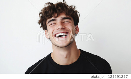 Enthusiastic young man with curly hair caught in a fit of contagious laughter, teeth showing against a plain white backdrop. 123291237