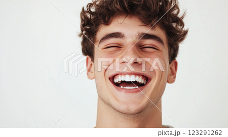 Smiling Teen: Headshot of a joyful young man with curly hair, eyes closed in laughter against a plain backdrop. Pure happiness on display. 123291262