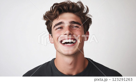 A young man radiates pure joy, his face alight with a contagious, unrestrained laugh against a clean, bright backdrop. Positivity shines. 123291263