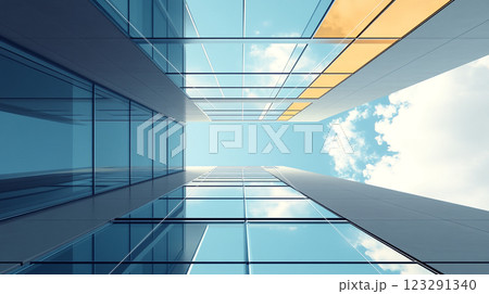 Looking up at modern office buildings featuring a glass facade reflecting the blue sky with white clouds. The sunlight illuminates the glass. 123291340