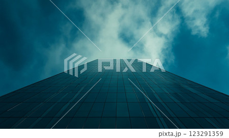 A towering skyscraper ascends towards a dramatic, cloudy sky, showcasing modern architecture against a backdrop of natural beauty. 123291359
