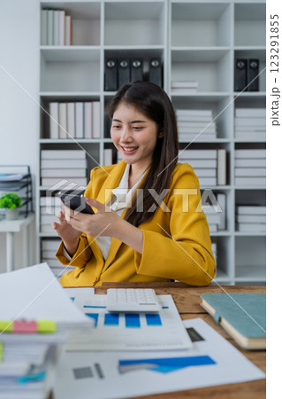 young businesswoman in a bright yellow suit smiling while using smartphone in a modern office environment 123291855