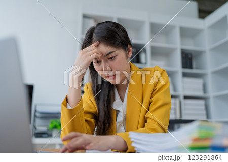 Stressed businesswoman in yellow blazer overwhelmed by work at a desk with papers and laptop in a modern office setting Stressed businesswoman in yellow blazer overwhelmed by work at a desk with papers and laptop in a modern office setting 123291864