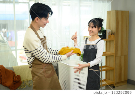 Happy young couple folding laundry together in living room. Home organization concept 123292099