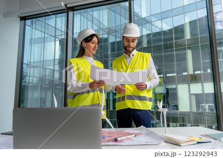 Two people in yellow vests and hard caps working together in the office 123292943