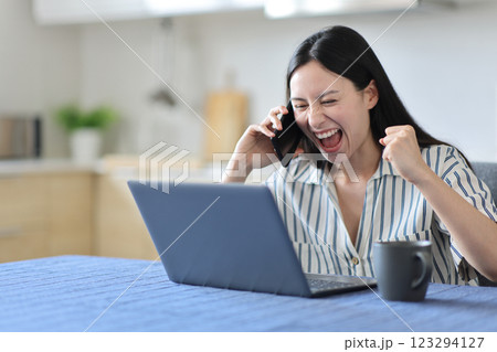 Excited asian woman talking on phone checking laptop 123294127