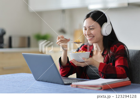 Happy asian student eating cereal e-learning in a kitchen Happy asian student eating cereal e-learning in a kitchen 123294128