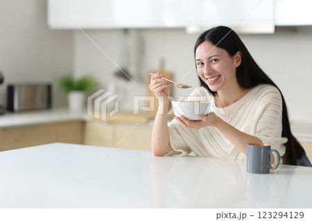 Happy asian woman eating cereals looking at camera in a kitchen 123294129